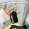A hand holds a black and silver keychain charm accessory bag with a gold clasp.