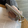 A hand holds a silver-toned zipper compact coin purse and key holder against a piece of paper.