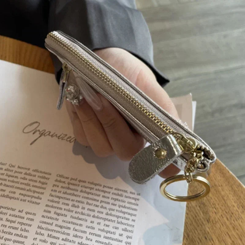 A hand holds a silver-toned zipper compact coin purse and key holder against a piece of paper.