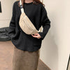 A person wearing a black sweater holds a beige corduroy crossbody waist bag with an adjustable strap.