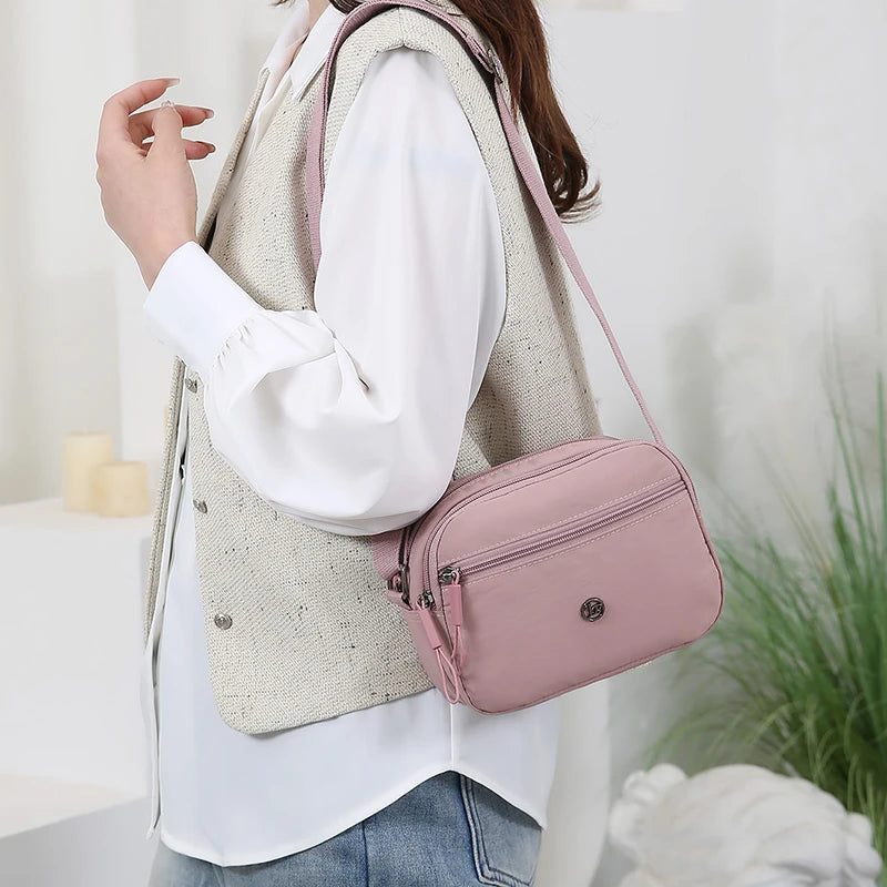 A woman wearing a beige vest and white shirt carrying a pink nylon crossbody bag.