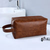 A brown portable PU leather cosmetic organizer bag resting on a white surface next to a sink.