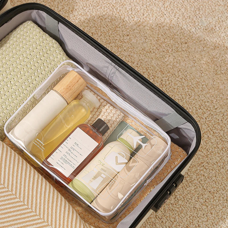 A clear PVC toiletry bag with a zipper closure containing various skincare products and a natural fiber lining.