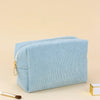 Light blue corduroy makeup organizer bag with a zipper lying on a beige surface.