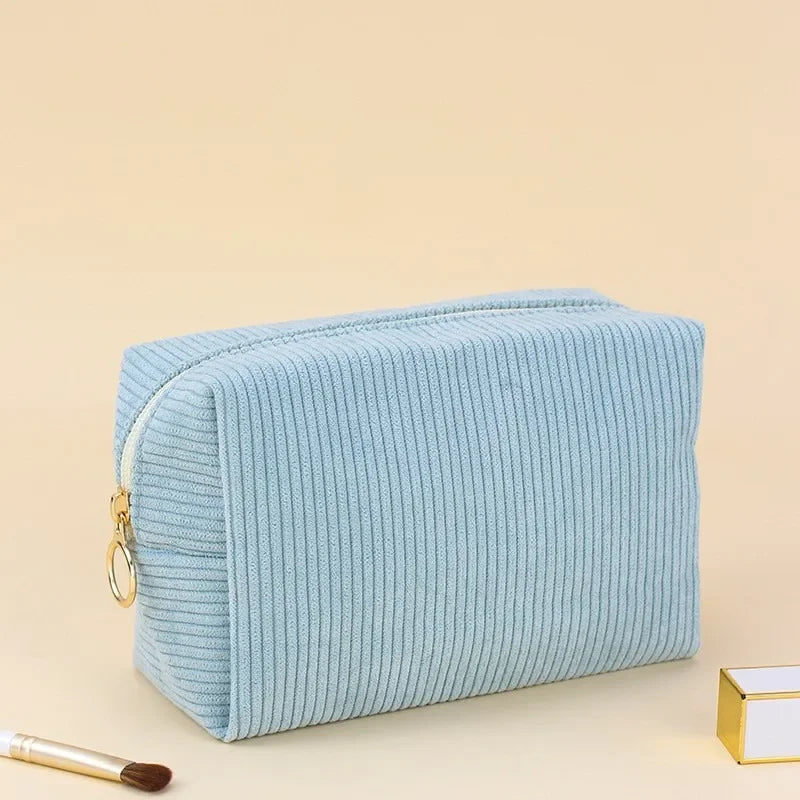 Light blue corduroy makeup organizer bag with a zipper lying on a beige surface.