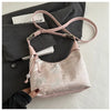 A light pink satin embroidered crossbody shoulder bag is displayed against a dark gray blazer and white book.