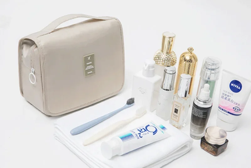 A beige waterproof makeup organizer and travel pouch with various cosmetic products displayed on a white surface.