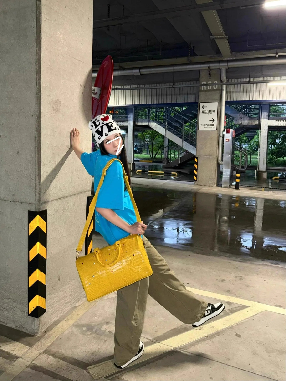 A person wearing a blue shirt and khaki pants is holding a yellow faux crocodile tote bag in an indoor public area.
