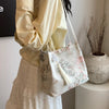 Bolso de hombro de seda jacquard retro color crema con bordado floral, sostenido por una persona con blusa amarillo claro