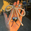 A hand holds a pearl necklace featuring a bowknot and a heart charm.