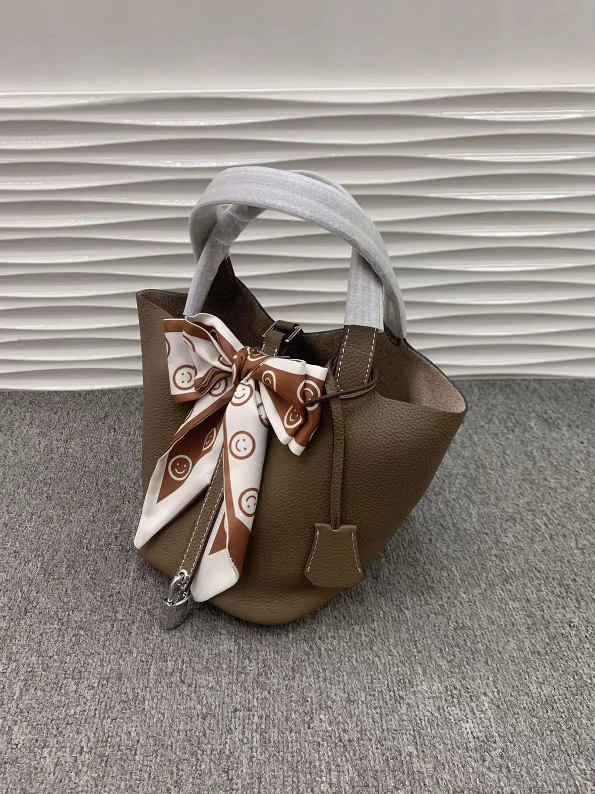 Braune Leder-Bucket-Tasche mit weiß-braunem gemusterten Bandverschluss auf grauem Untergrund