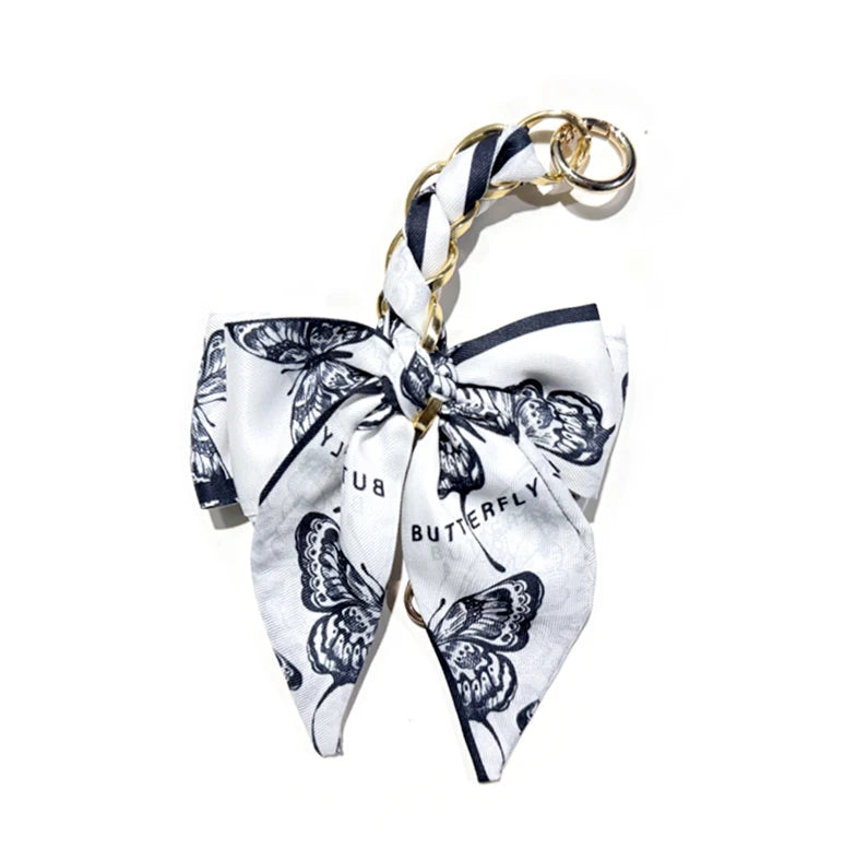 A white fabric bow bag chain strap extension featuring black butterfly print.