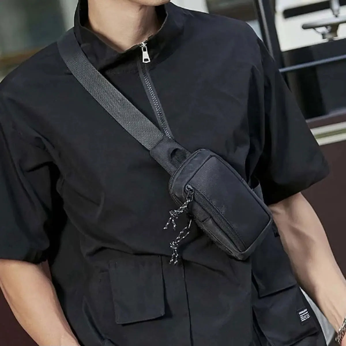 Ein Mann trägt ein schwarzes kurzärmeliges Hemd mit einer schwarzen Crossbody-Messenger-Tasche über der Schulter.