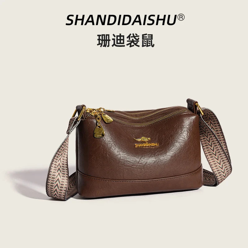A brown luxury PU leather crossbody handbag with gold hardware and a patterned strap.