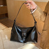 A woman holds a black retro PU leather underarm bag against a light wooden background.