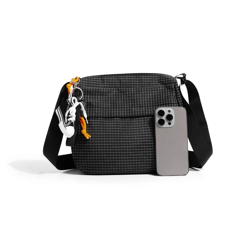 A black plaid crossbody shoulder bag with a silver phone attached and orange keychain.