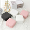A collection of pink and white compact leather jewelry travel boxes displayed on a white textured fabric next to a white stor