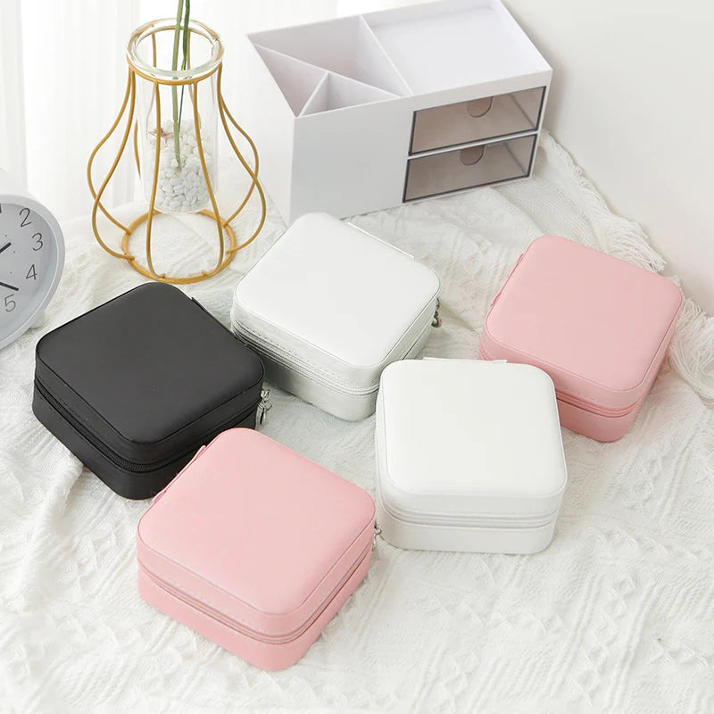 A collection of pink and white compact leather jewelry travel boxes displayed on a white textured fabric next to a white stor