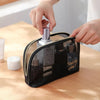 A hand is placing a glass bottle into a black mesh travel cosmetic storage pouch.