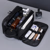 A black PU leather travel toiletry bag with multiple organizer pockets and grooming tools is shown on a gray surface.