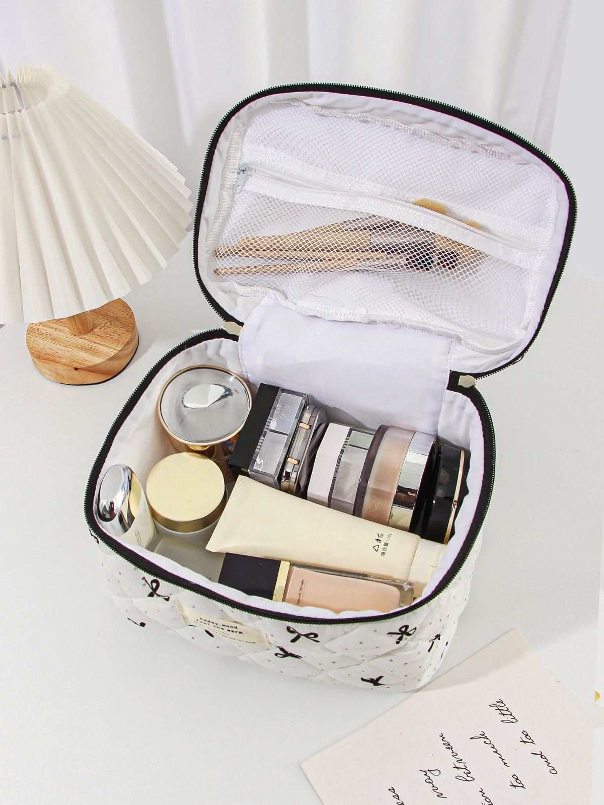 An open quilted makeup bag with various cosmetic products inside, resting on a white surface.