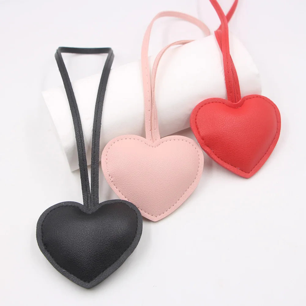 Three heart-shaped PU leather keychains in pink, red, and black with attached loops