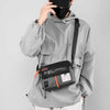 A person wearing a gray hooded jacket holds a black waterproof nylon crossbody bag.