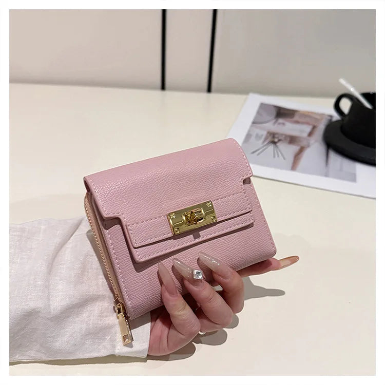 A pink leather card holder with a gold clasp is held next to a white linen cloth on a light surface.