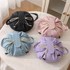 A flat lay of four instant-open makeup organizer bags in black, pink, light blue, and purple on a white table.