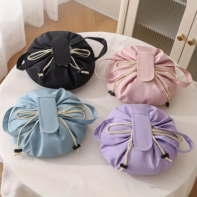 A flat lay of four instant-open makeup organizer bags in black, pink, light blue, and purple on a white table.