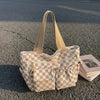 A beige and cream checkered corduroy tote bag resting on asphalt with a stack of books.