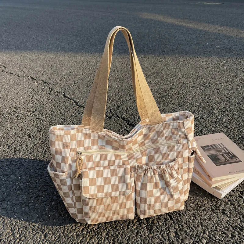 A beige and cream checkered corduroy tote bag resting on asphalt with a stack of books.