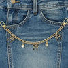 A close-up of a denim jean pocket featuring a gold chain necklace with pearl charms.