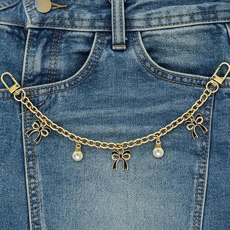A close-up of a denim jean pocket featuring a gold chain necklace with pearl charms.
