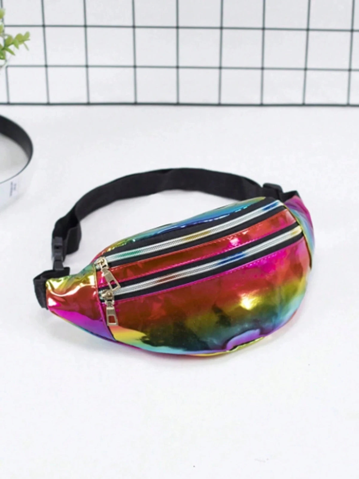 A holographic sequin waist bag with a black adjustable strap, displayed on a white surface.