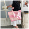 A person holds a pink and white striped waterproof PVC shoulder tote bag in front of a glass door.
