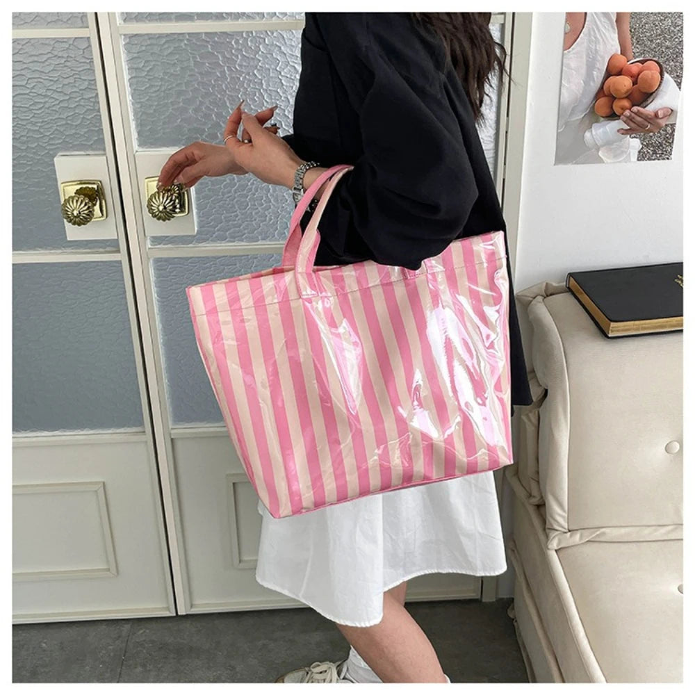 A person holds a pink and white striped waterproof PVC shoulder tote bag in front of a glass door.