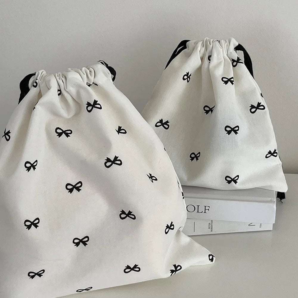 A white canvas makeup bag with black bowknot detailing is shown in a close-up view.