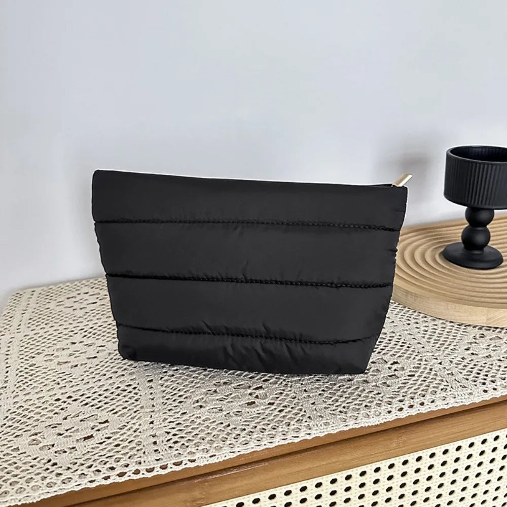 A black quilted cosmetic travel bag resting on a woven mat.