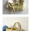 Sac à main en cuir PU beige clair décontracté avec des anses en tan, accroché sur un fond blanc.