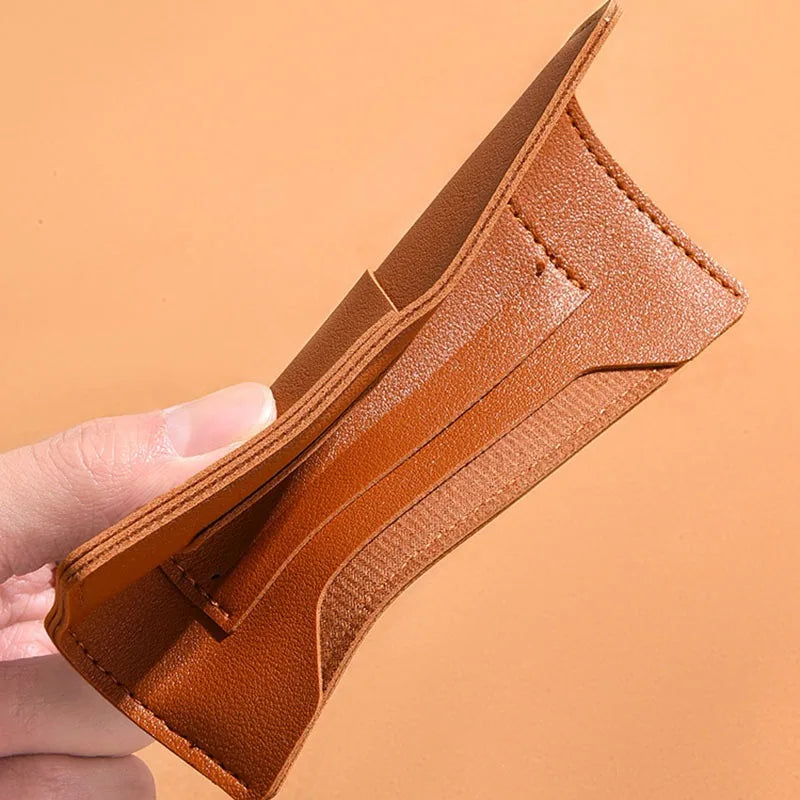 Une main tient un portefeuille de voyage fin en cuir marron pour passeport et documents.