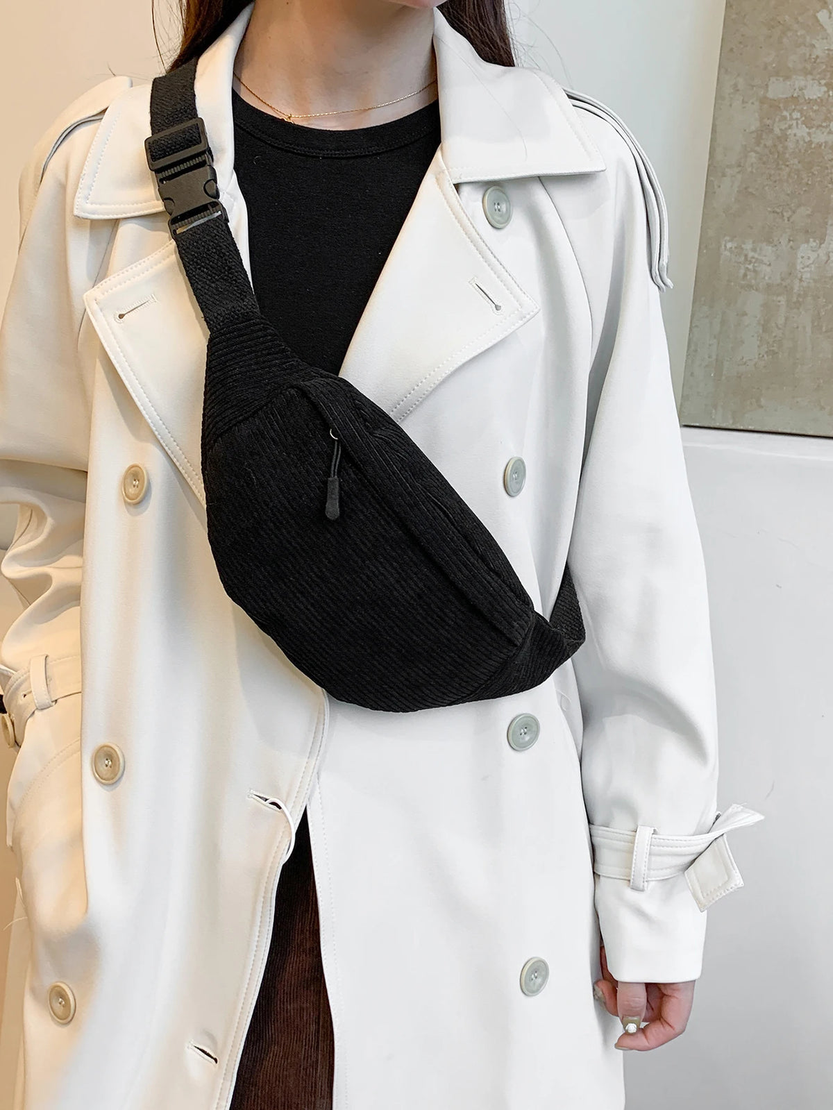 A woman wearing a white trench coat and black top, carrying a black nylon crossbody sling bag.