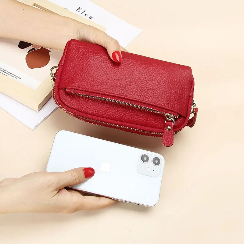 A hand holds a red leather double-zip wristlet wallet next to a white smartphone on a light background.