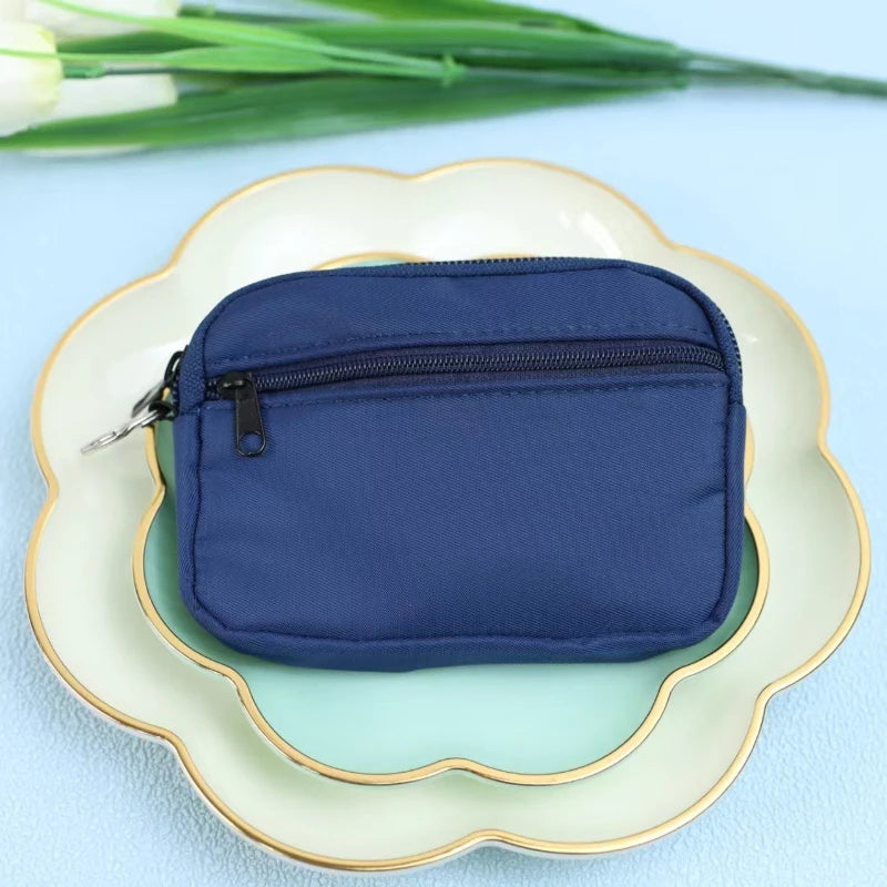 A navy blue nylon mini coin purse with a double zipper is placed on a light green plate.