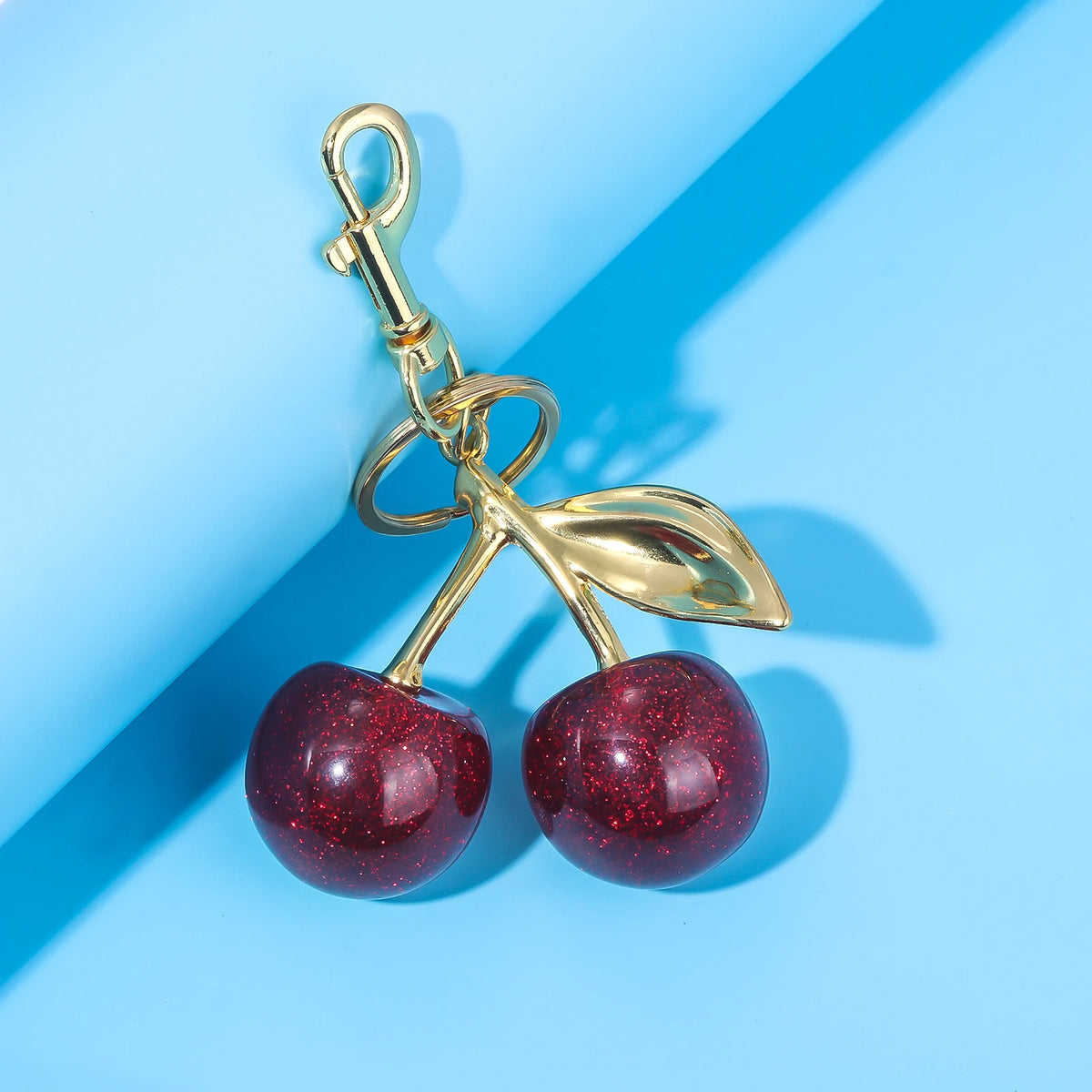 Gold-toned keychain featuring a leaf and two shiny red crystal cherry fruit charms.