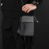 A black Oxford chest bag is shown being held by a person wearing a black jacket and pants.