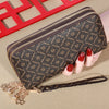 Cartera con cremallera de imitación de cuero marrón oscuro y diseño estampado junto a un marco rojo y una mano.
