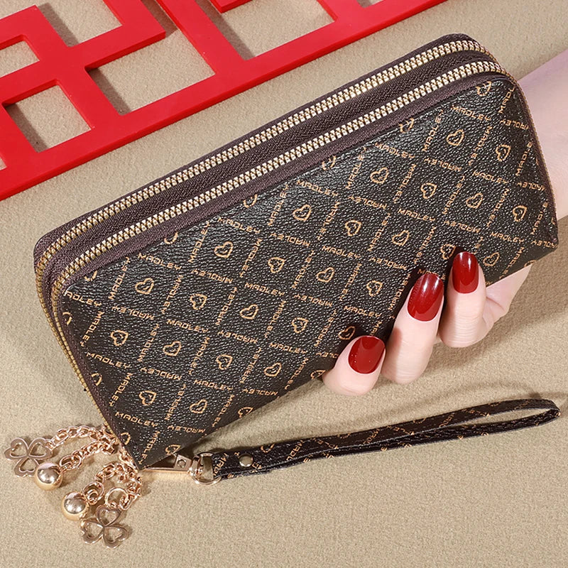 Cartera con cremallera de imitación de cuero marrón oscuro y diseño estampado junto a un marco rojo y una mano.