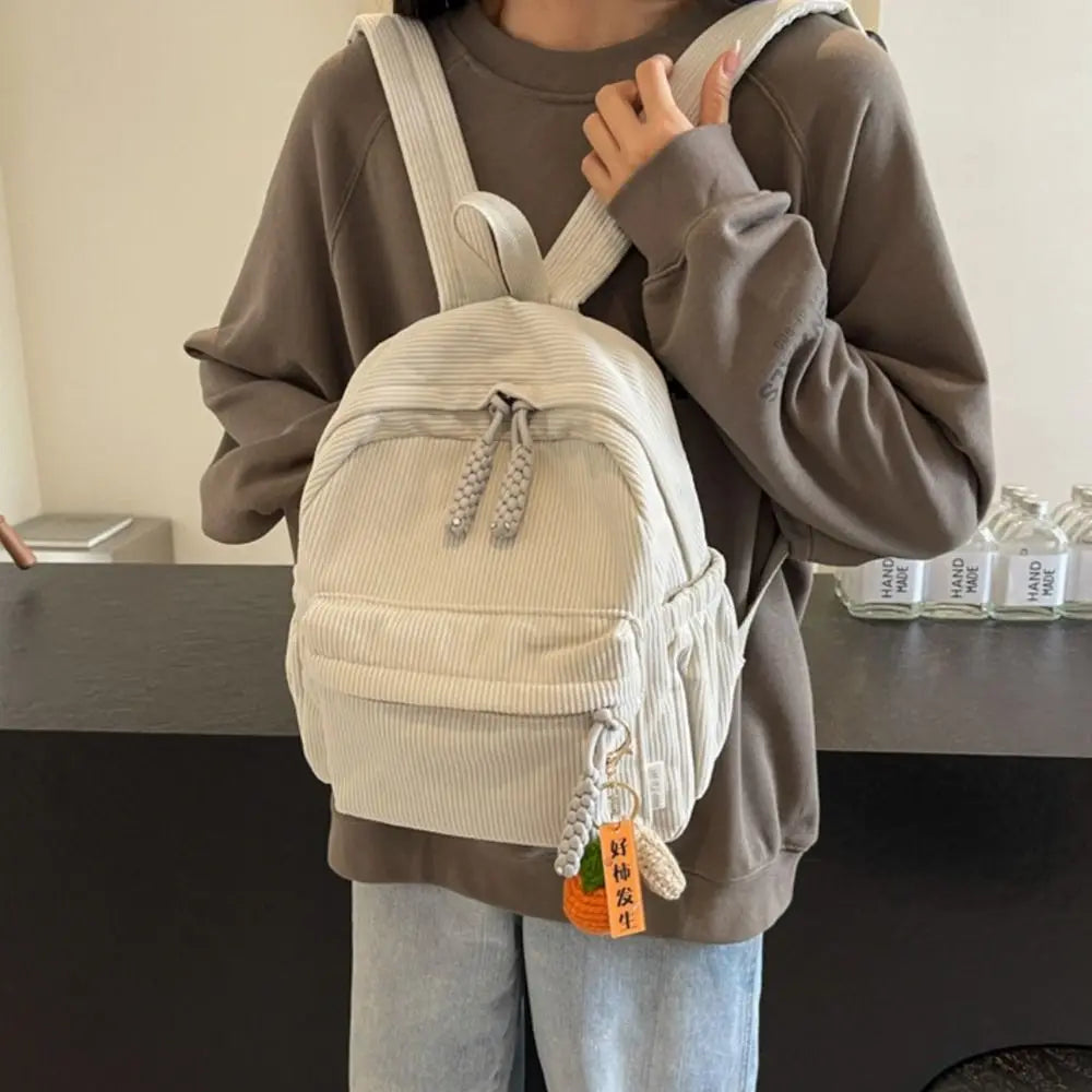 A person wearing a beige lightweight corduroy daily backpack over a brown sweatshirt.