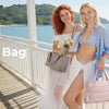 Zwei Frauen stehen auf einem Holzsteg am Meer und halten und präsentieren eine voluminöse Tasche.